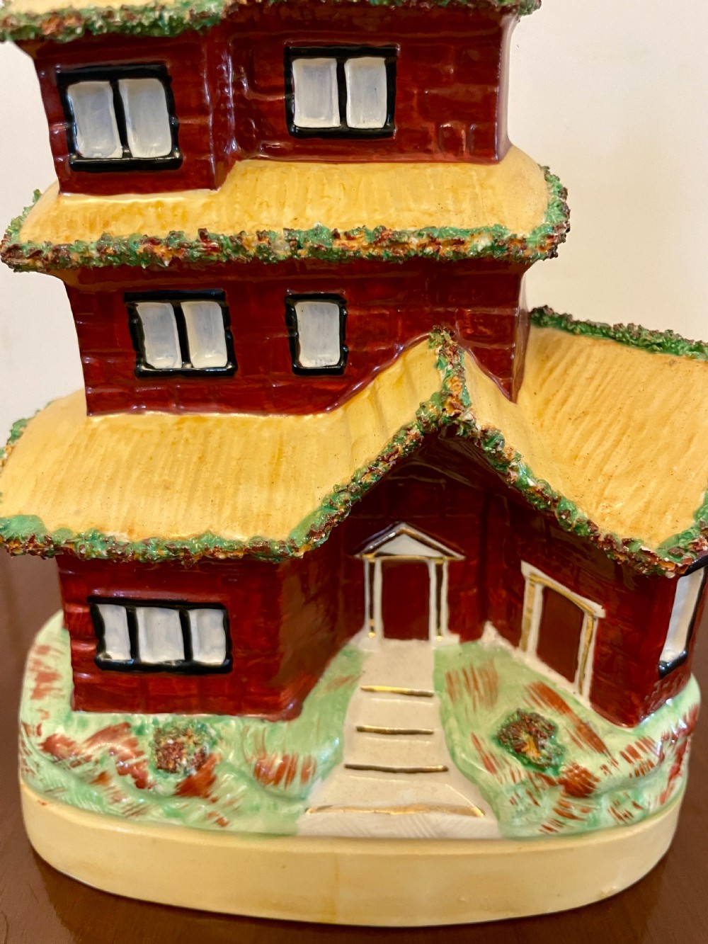 A Victorian Staffordshire pottery flatback figurine depicting a multi-storey terracotta red house with a yellow thatched roof, green encrusted foliage trim, and two chimneys. View III