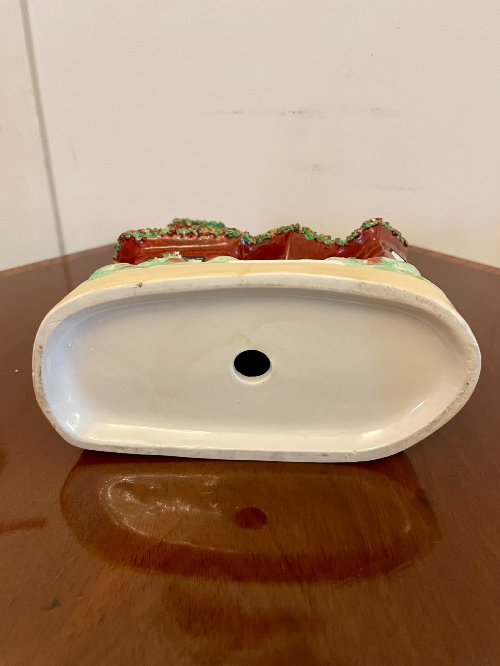 A Victorian Staffordshire pottery flatback figurine depicting a multi-storey terracotta red house with a yellow thatched roof, green encrusted foliage trim, and two chimneys. View VI