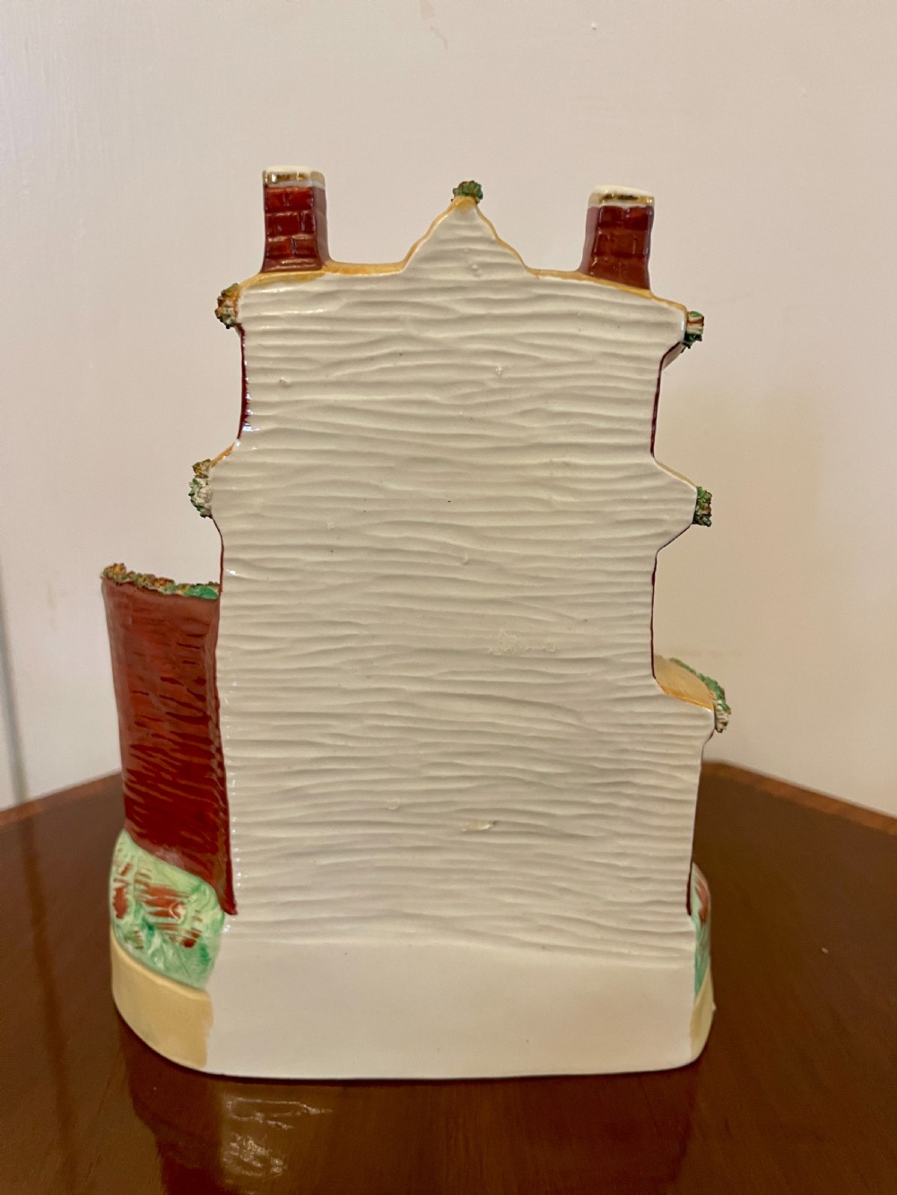 A Victorian Staffordshire pottery flatback figurine depicting a multi-storey terracotta red house with a yellow thatched roof, green encrusted foliage trim, and two chimneys. View VII