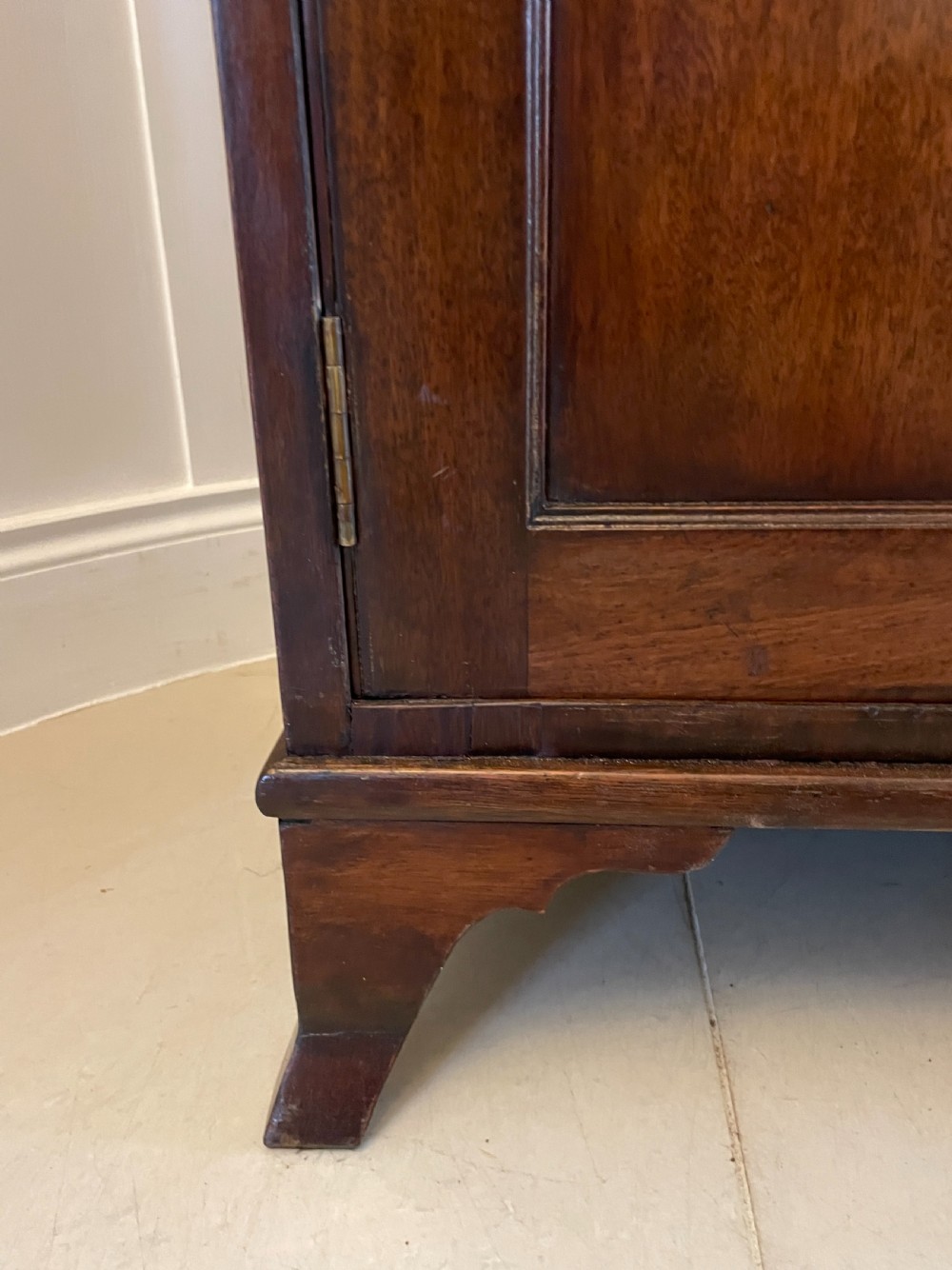A George III mahogany secretaire desk featuring top drawers with brass ring handles over a two-door panelled cupboard base resting on bracket feet. View II