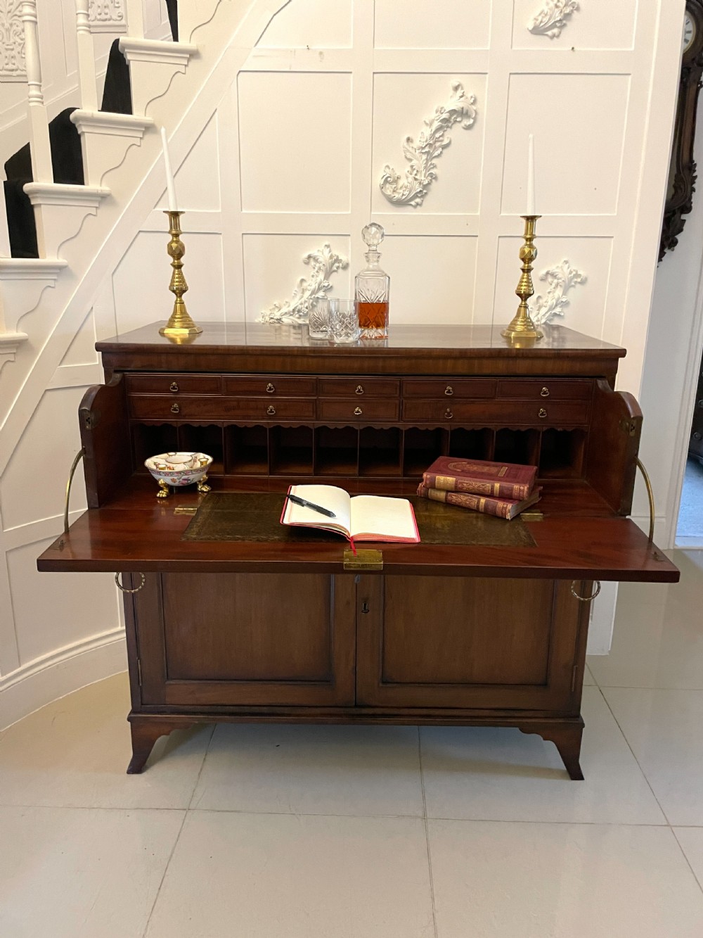 A George III mahogany secretaire desk featuring top drawers with brass ring handles over a two-door panelled cupboard base resting on bracket feet. View VI