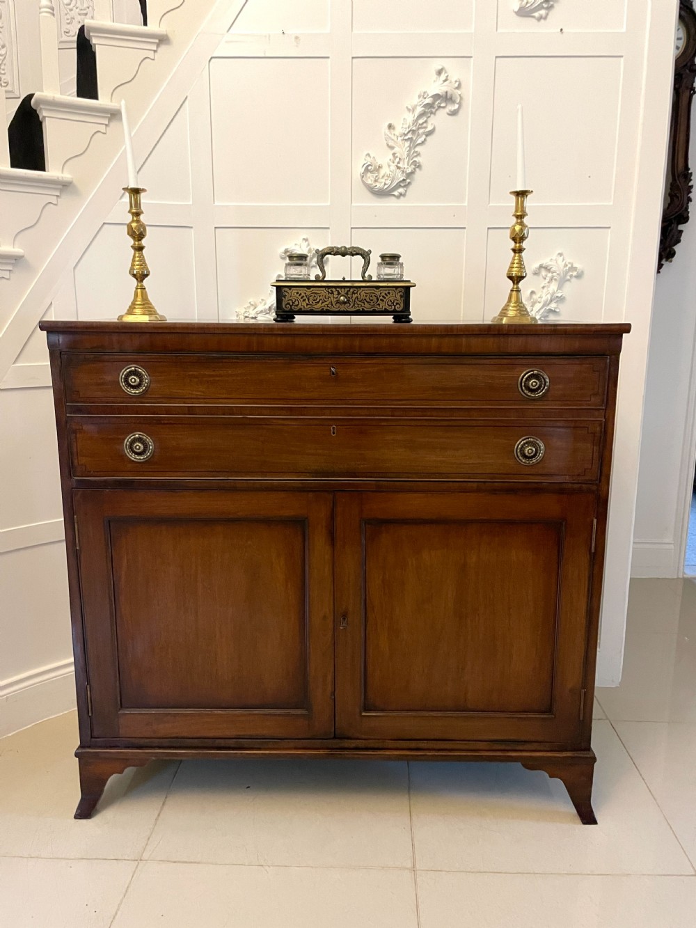 A George III mahogany secretaire desk featuring top drawers with brass ring handles over a two-door panelled cupboard base resting on bracket feet. View VII