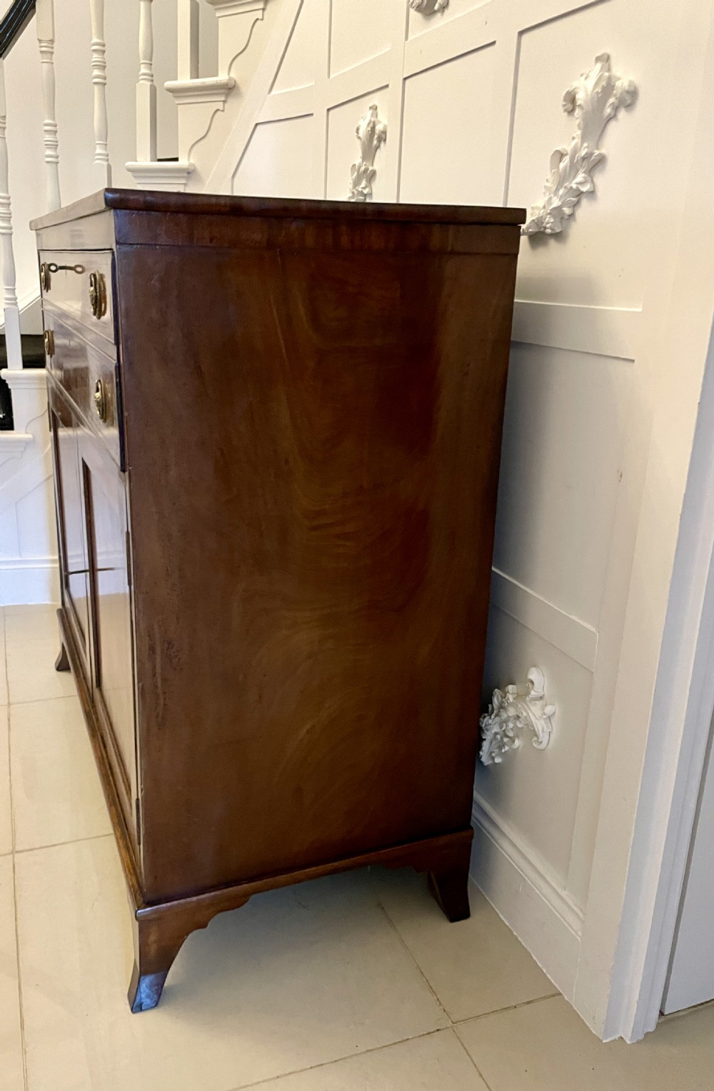 A George III mahogany secretaire desk featuring top drawers with brass ring handles over a two-door panelled cupboard base resting on bracket feet. View VIII