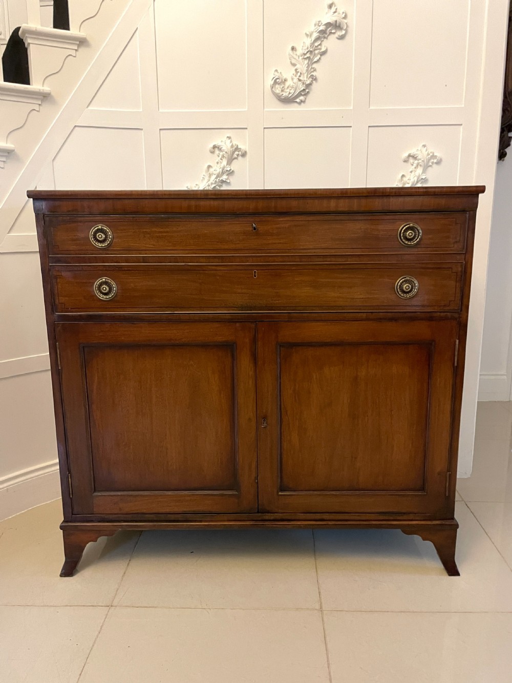 A George III mahogany secretaire desk featuring top drawers with brass ring handles over a two-door panelled cupboard base resting on bracket feet. View XII