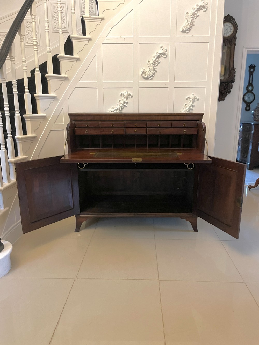 A George III mahogany secretaire desk featuring top drawers with brass ring handles over a two-door panelled cupboard base resting on bracket feet. View XIII