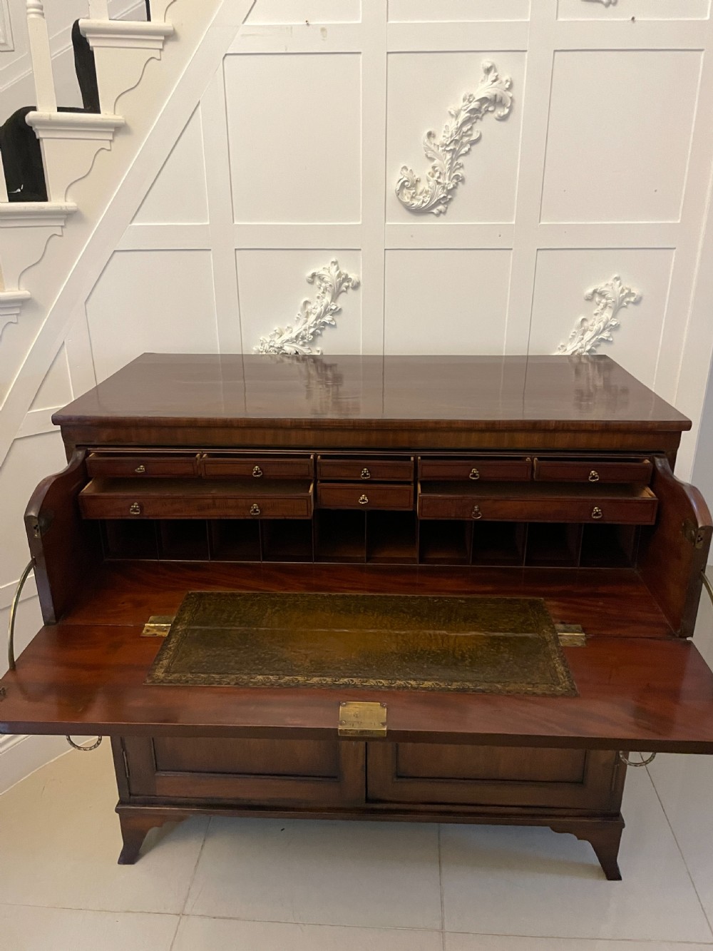 A George III mahogany secretaire desk featuring top drawers with brass ring handles over a two-door panelled cupboard base resting on bracket feet. View XVI