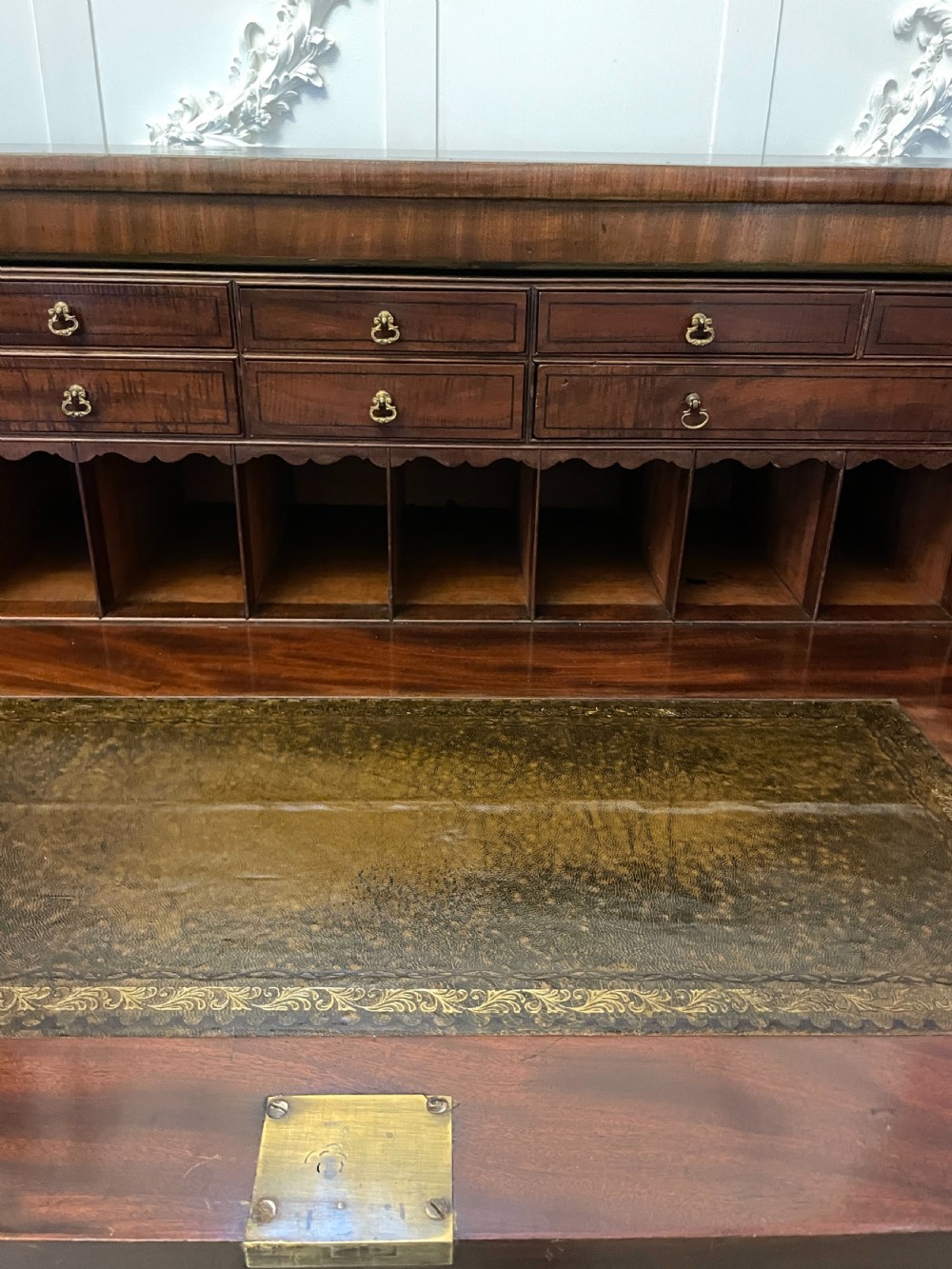 A George III mahogany secretaire desk featuring top drawers with brass ring handles over a two-door panelled cupboard base resting on bracket feet. View XX