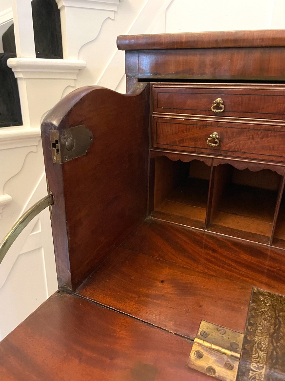 A George III mahogany secretaire desk featuring top drawers with brass ring handles over a two-door panelled cupboard base resting on bracket feet. View XXI