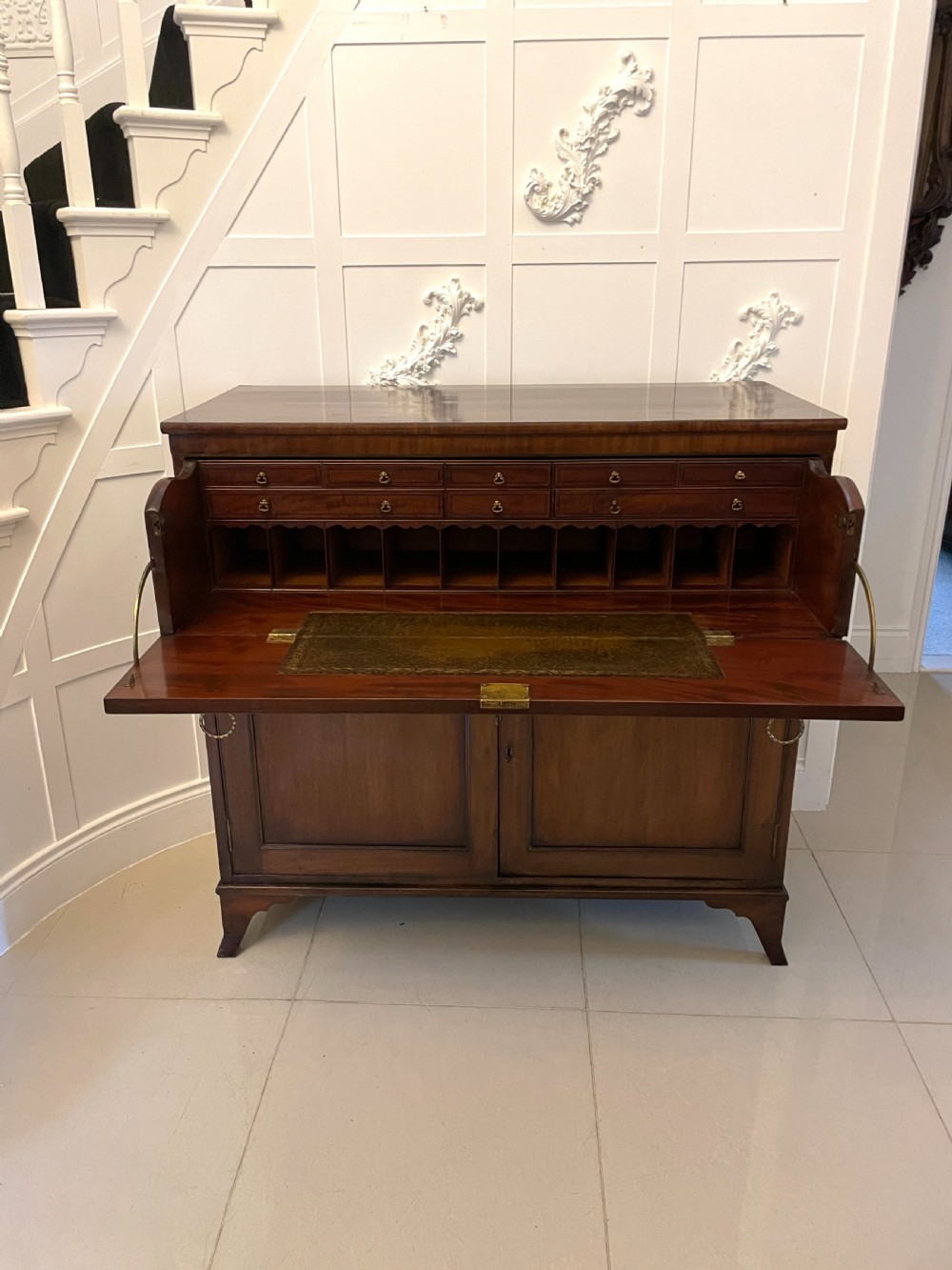 A George III mahogany secretaire desk featuring top drawers with brass ring handles over a two-door panelled cupboard base resting on bracket feet. View XXII