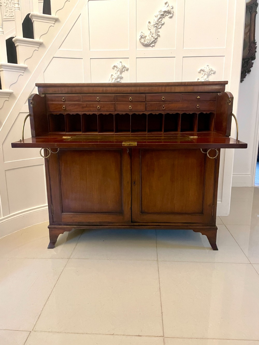 A George III mahogany secretaire desk featuring top drawers with brass ring handles over a two-door panelled cupboard base resting on bracket feet. View XXIII
