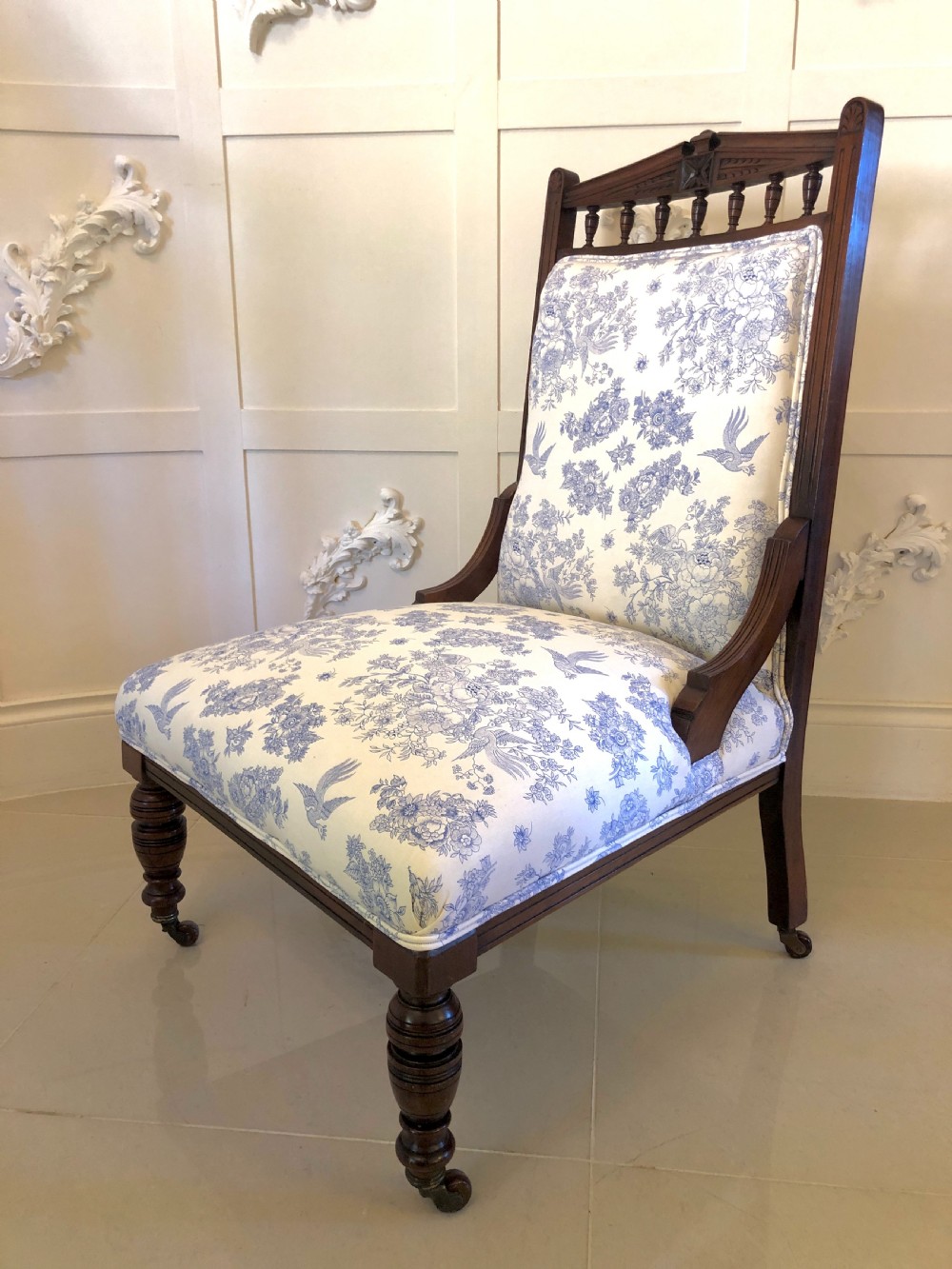 A Victorian carved walnut ladies chair featuring blue and white floral fabric upholstery, turned front legs with castors, and a spindle crest rail.
