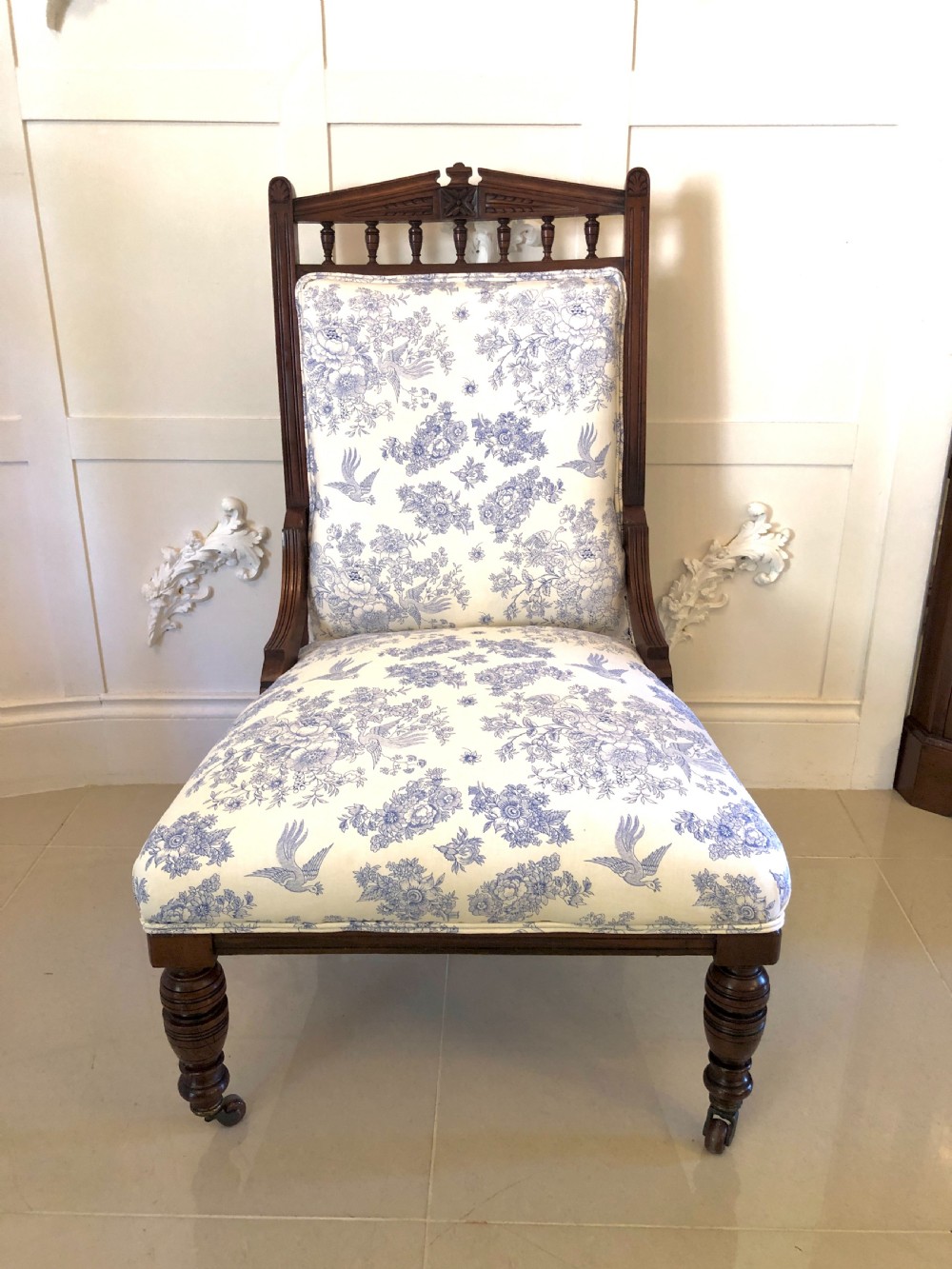 A Victorian carved walnut ladies chair featuring blue and white floral fabric upholstery, turned front legs with castors, and a spindle crest rail. View XIII