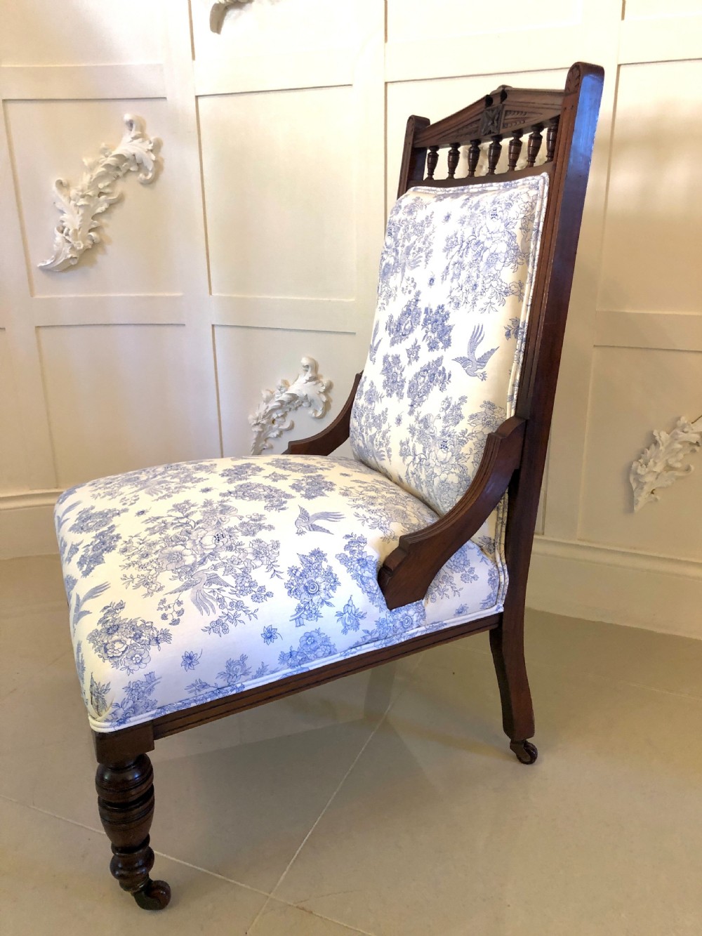 A Victorian carved walnut ladies chair featuring blue and white floral fabric upholstery, turned front legs with castors, and a spindle crest rail. View XIV