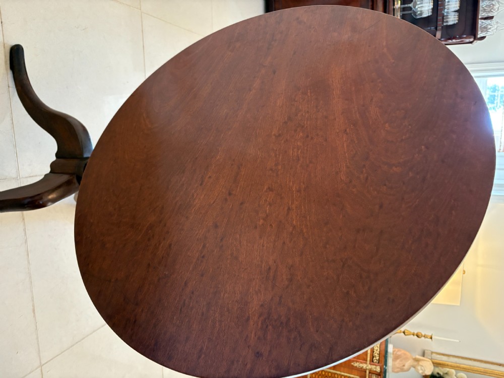 A George III circular plum pudding mahogany tilt-top table shown tilted vertically on a turned column stem with tripod legs. View III