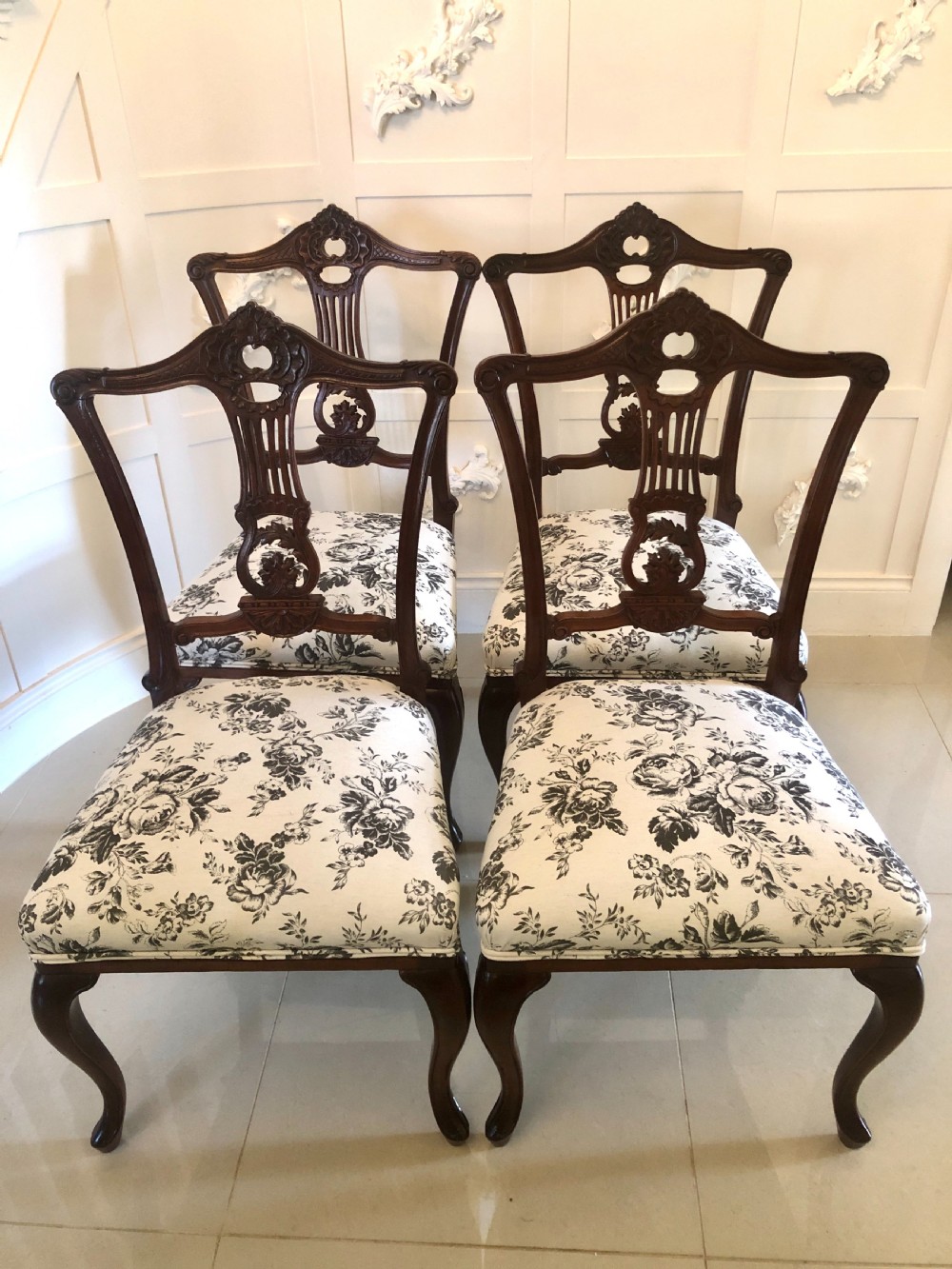 A set of four dark mahogany Victorian dining chairs featuring openwork carved back splats, cabriole front legs, and seats upholstered in a monochrome floral fabric.