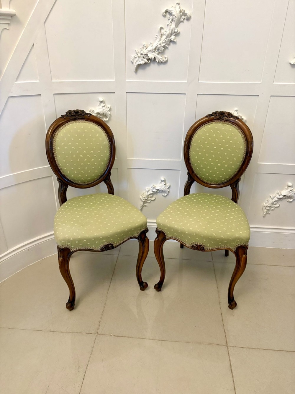 A pair of antique Victorian walnut side chairs featuring curved cabriole legs and green patterned upholstery.