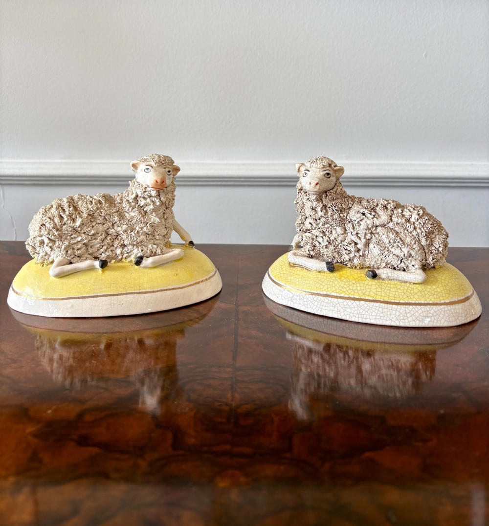 A pair of antique Staffordshire pottery sheep figures resting on yellow bases with textured wool coats and hand-painted facial features.