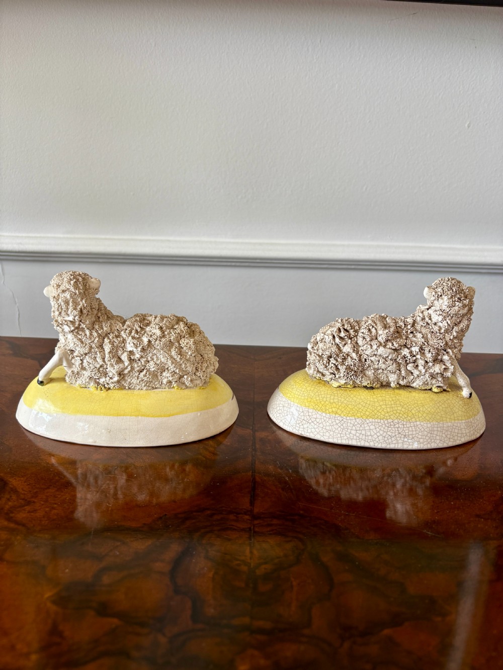 A pair of antique Staffordshire pottery sheep figures resting on yellow bases with textured wool coats and hand-painted facial features. View VII