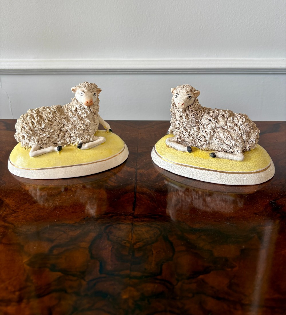 A pair of antique Staffordshire pottery sheep figures resting on yellow bases with textured wool coats and hand-painted facial features. View VIII
