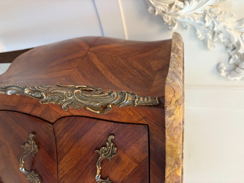 A pair of French Louis XV style kingwood bedside cabinets featuring shaped variegated marble tops, serpentine two-drawer fronts with marquetry inlay, gilt bronze mounts, and slender cabriole legs. View X