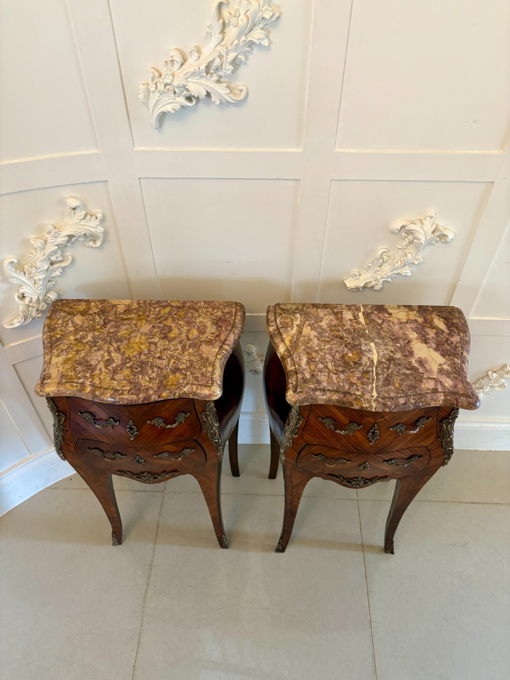 A pair of French Louis XV style kingwood bedside cabinets featuring shaped variegated marble tops, serpentine two-drawer fronts with marquetry inlay, gilt bronze mounts, and slender cabriole legs. View XIII