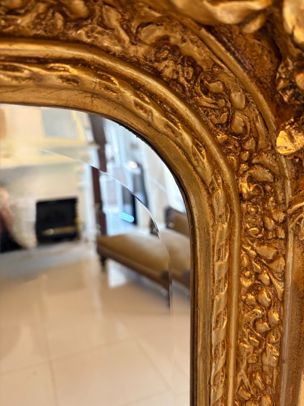 A large rectangular wall mirror featuring an ornate gilded frame decorated with carved floral scrolls and two cherub figures atop the crest. View III