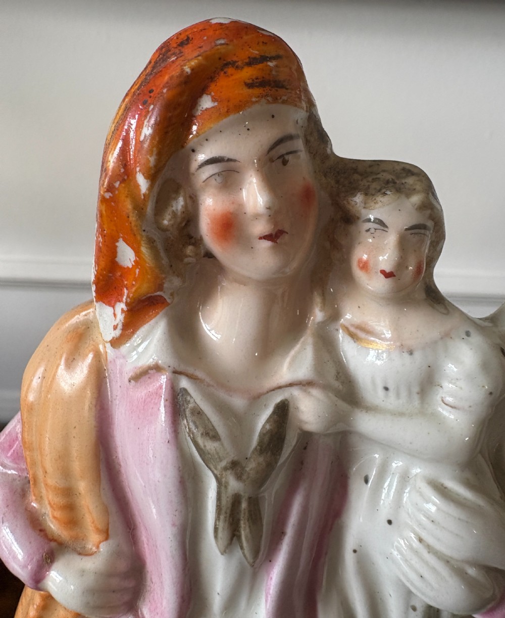 Victorian Staffordshire earthenware figurine depicting a man in a tartan kilt holding a child next to a woman, painted in polychrome glazes on a moulded base. View VI