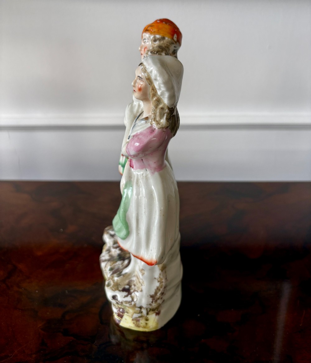 Victorian Staffordshire earthenware figurine depicting a man in a tartan kilt holding a child next to a woman, painted in polychrome glazes on a moulded base. View IX
