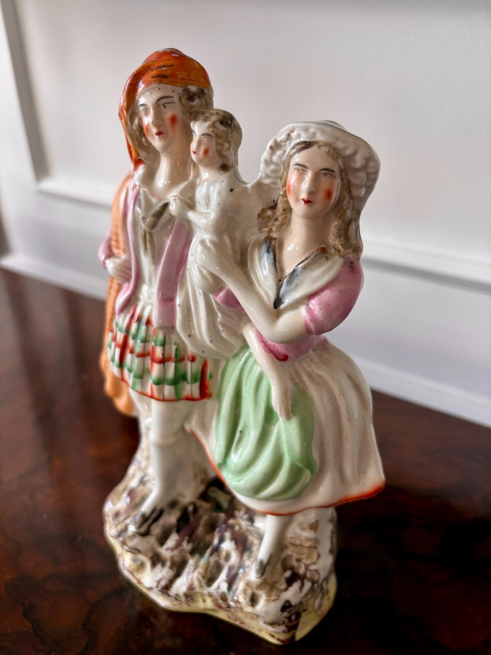 Victorian Staffordshire earthenware figurine depicting a man in a tartan kilt holding a child next to a woman, painted in polychrome glazes on a moulded base. View X