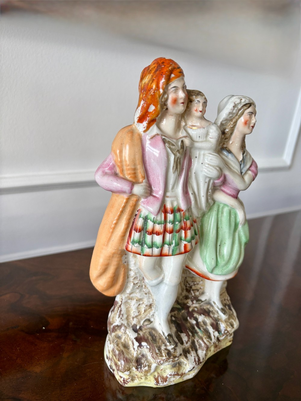 Victorian Staffordshire earthenware figurine depicting a man in a tartan kilt holding a child next to a woman, painted in polychrome glazes on a moulded base. View XI