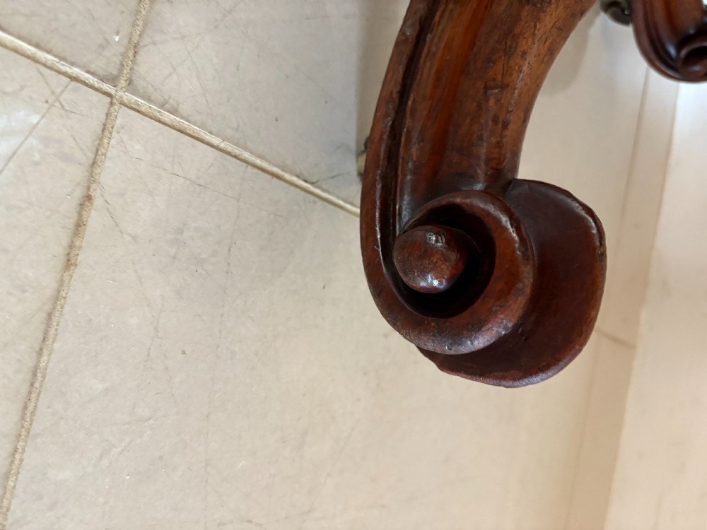 An antique Victorian oval mahogany dining table featuring crossbanded satinwood inlay, shown tilted vertically on a carved quadruped base with scroll feet and brass castors. View X