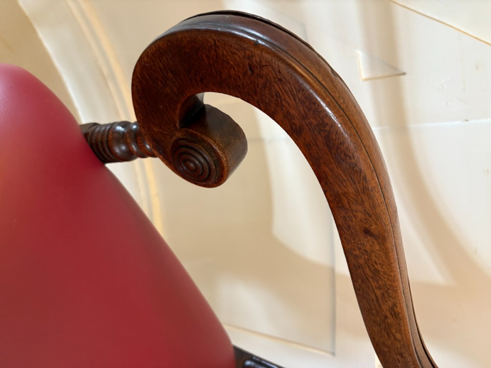 A pair of George III mahogany desk chairs featuring scroll arms, carved back splats, turned front legs, and red leather seats. View VIII