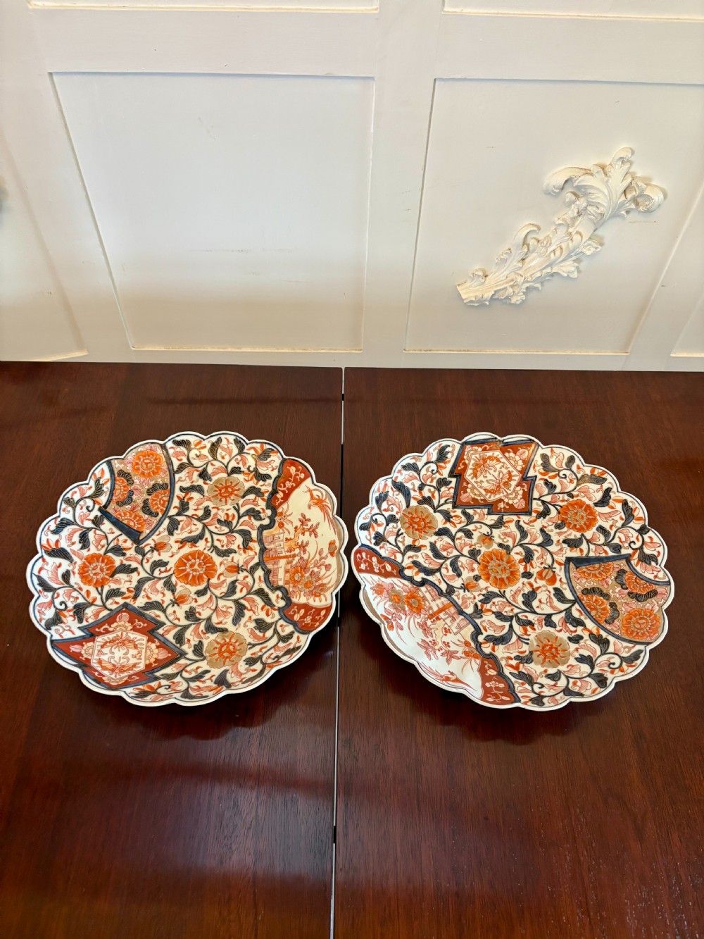 A pair of circular Japanese Imari porcelain plates with scalloped edges, decorated in hand-painted orange, terracotta, blue, and gold floral patterns.