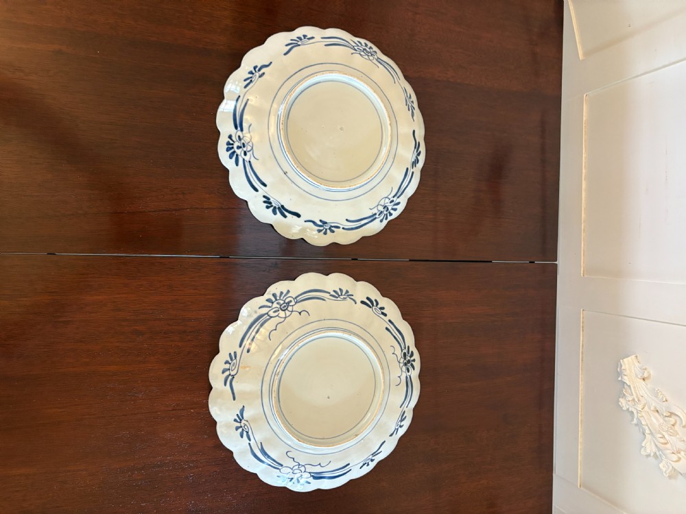 A pair of circular Japanese Imari porcelain plates with scalloped edges, decorated in hand-painted orange, terracotta, blue, and gold floral patterns. View V
