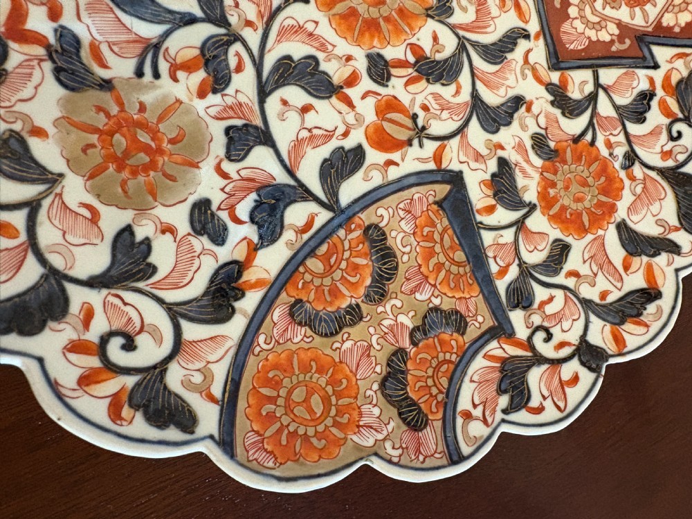 A pair of circular Japanese Imari porcelain plates with scalloped edges, decorated in hand-painted orange, terracotta, blue, and gold floral patterns. View VI