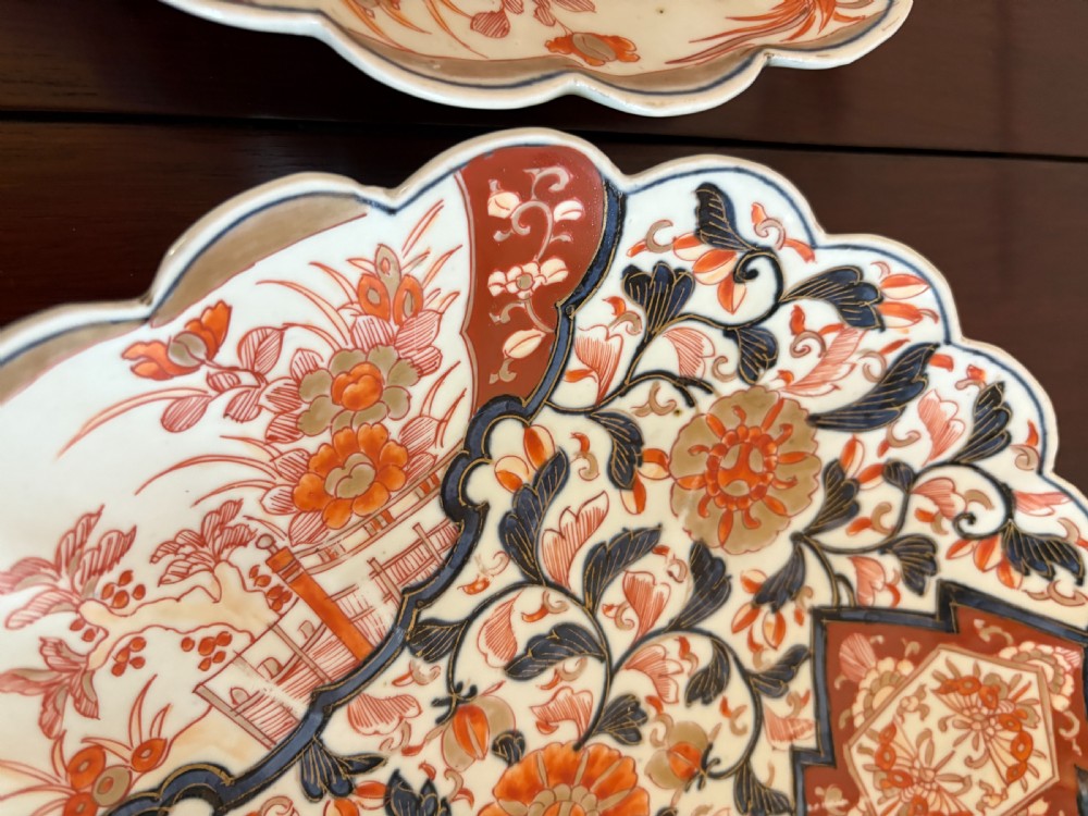 A pair of circular Japanese Imari porcelain plates with scalloped edges, decorated in hand-painted orange, terracotta, blue, and gold floral patterns. View VII