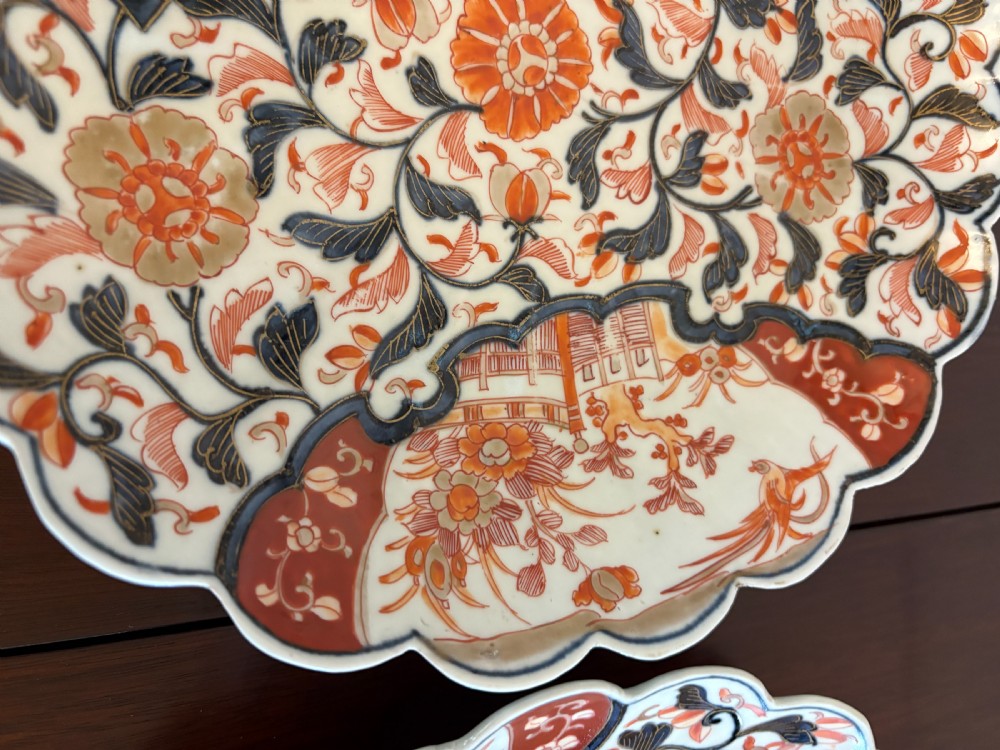 A pair of circular Japanese Imari porcelain plates with scalloped edges, decorated in hand-painted orange, terracotta, blue, and gold floral patterns. View VIII