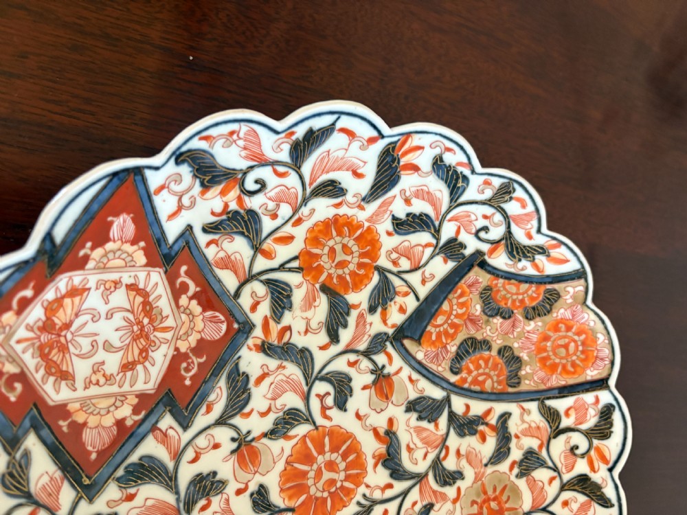 A pair of circular Japanese Imari porcelain plates with scalloped edges, decorated in hand-painted orange, terracotta, blue, and gold floral patterns. View IX