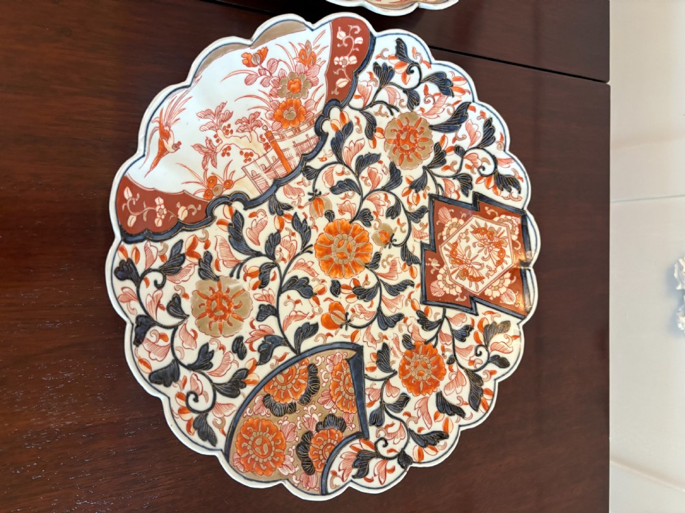 A pair of circular Japanese Imari porcelain plates with scalloped edges, decorated in hand-painted orange, terracotta, blue, and gold floral patterns. View XIII