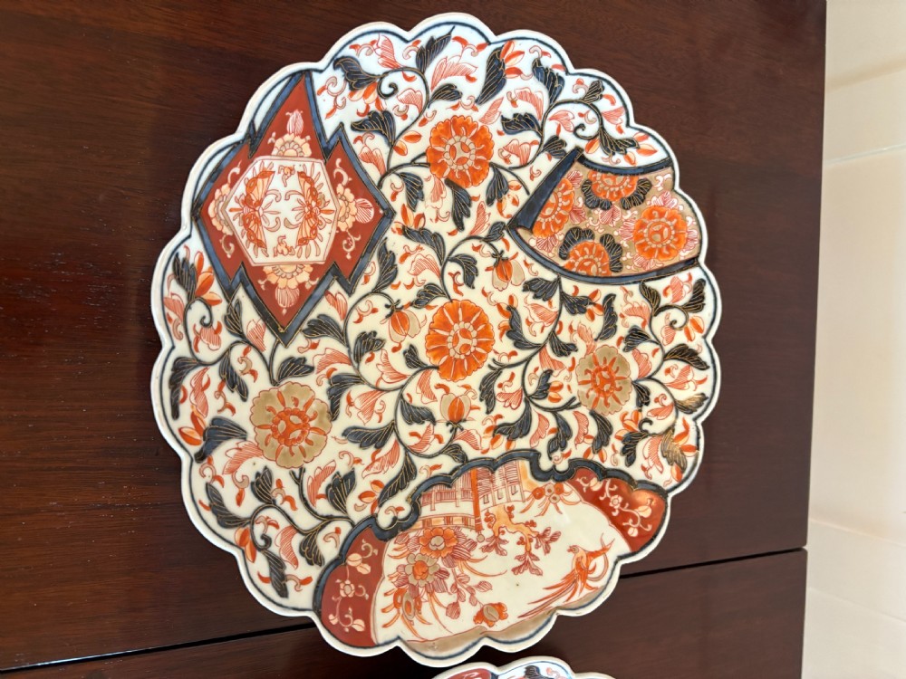 A pair of circular Japanese Imari porcelain plates with scalloped edges, decorated in hand-painted orange, terracotta, blue, and gold floral patterns. View XIV