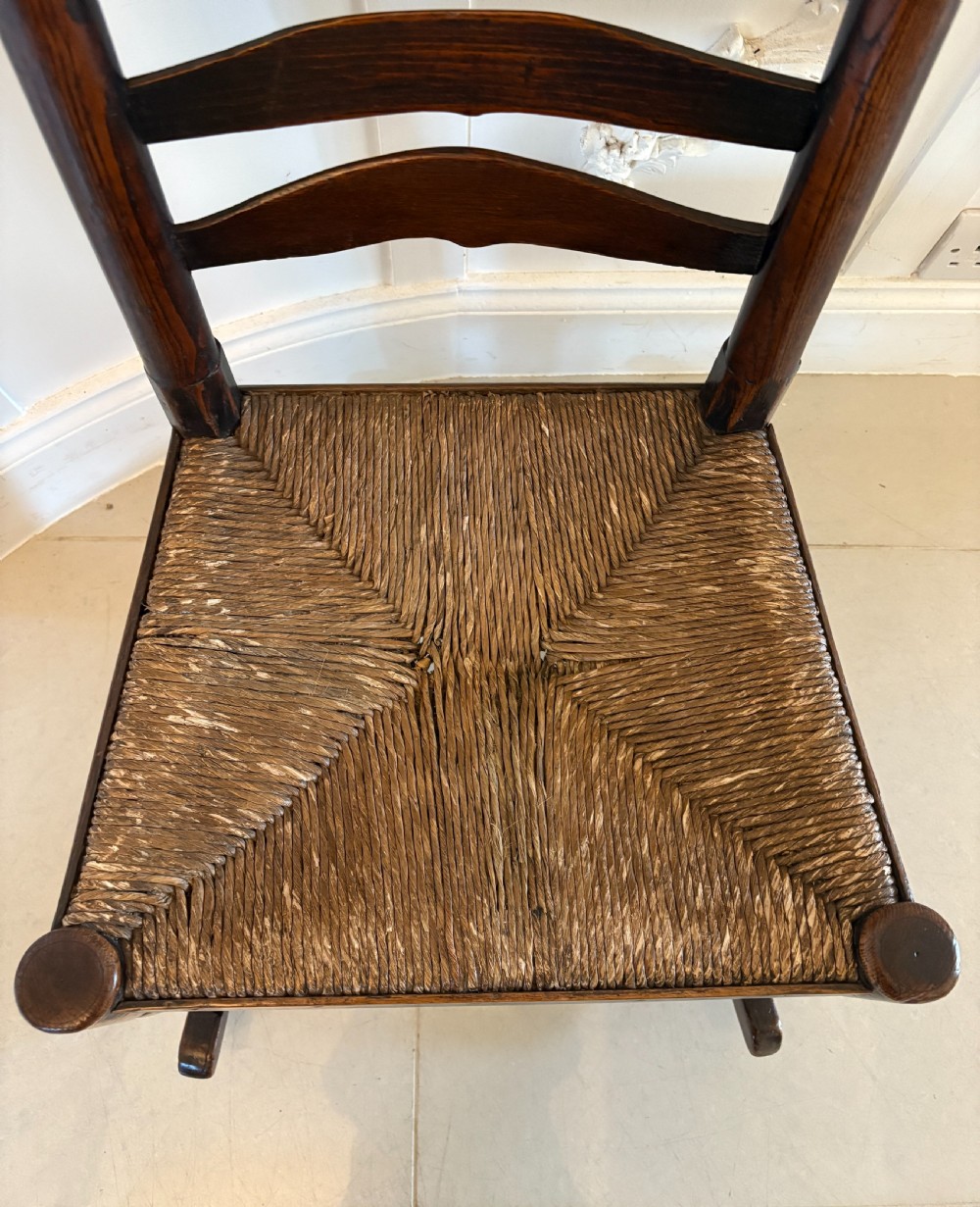 An 18th-century dark oak ladder back rocking chair featuring five shaped horizontal back slats, a woven rush seat, turned front legs, and wooden rockers. View VIII