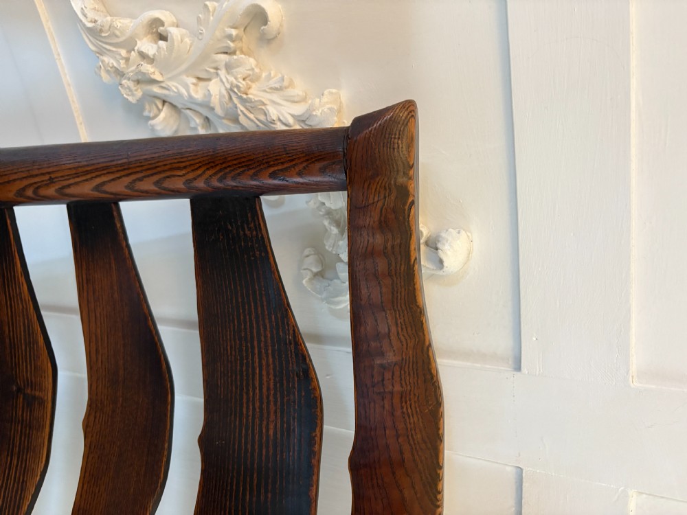 An 18th-century dark oak ladder back rocking chair featuring five shaped horizontal back slats, a woven rush seat, turned front legs, and wooden rockers. View XI