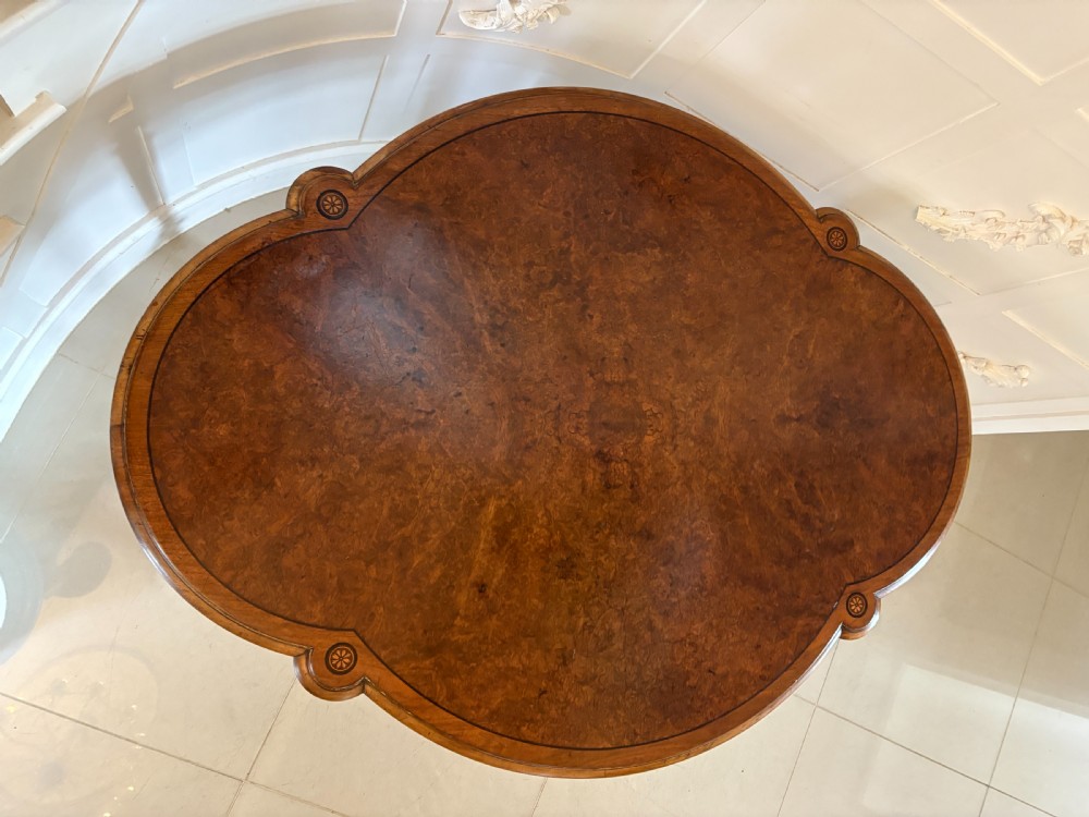 A Victorian burr walnut centre table with a lobed shaped top, inlaid crossbanding, turned legs, and an X-form stretcher on castors. View XI