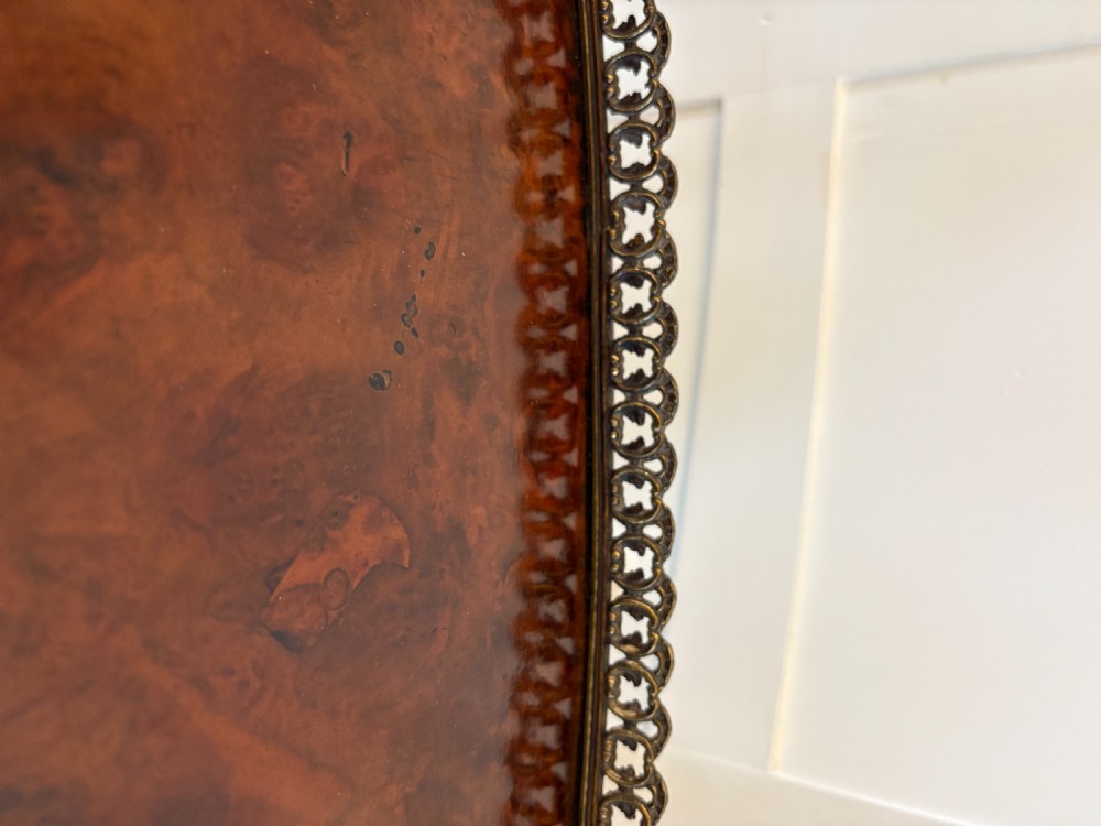 A Victorian three-tiered burr walnut whatnot featuring serpentine shelves, turned spindle supports, a pierced brass top gallery, and a base drawer on brass castors. View X
