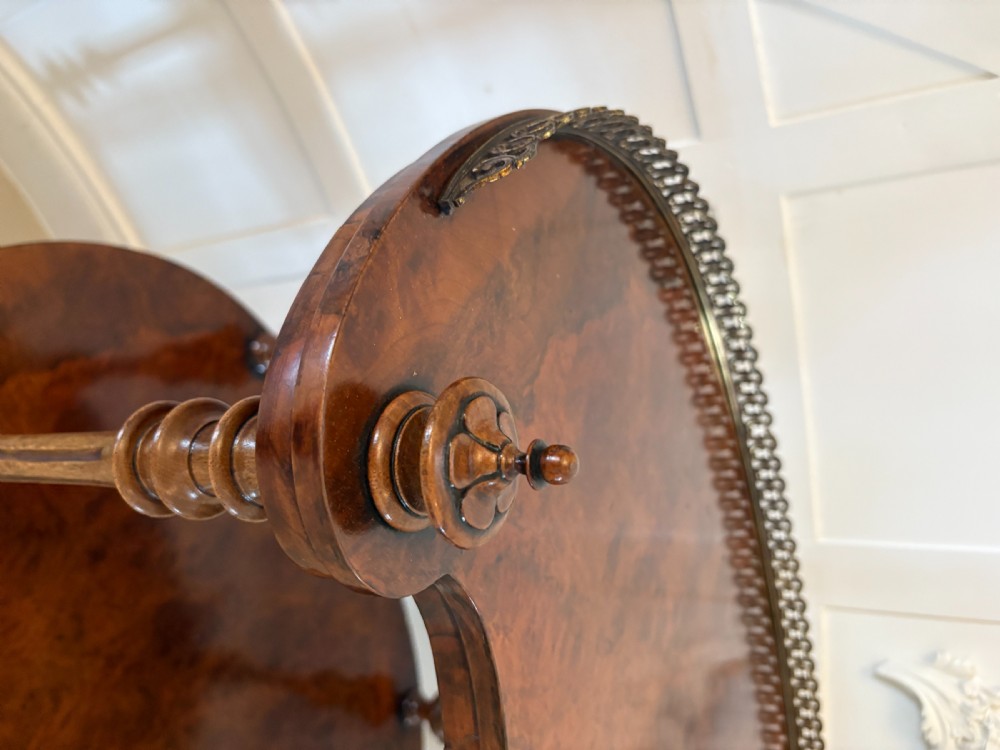 A Victorian three-tiered burr walnut whatnot featuring serpentine shelves, turned spindle supports, a pierced brass top gallery, and a base drawer on brass castors. View XI