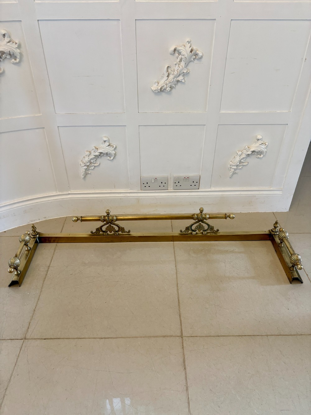 A Victorian brass fireplace fender featuring a low moulded base, fluted corner finials, and an elevated tool rail supported by scrolling brackets. View II