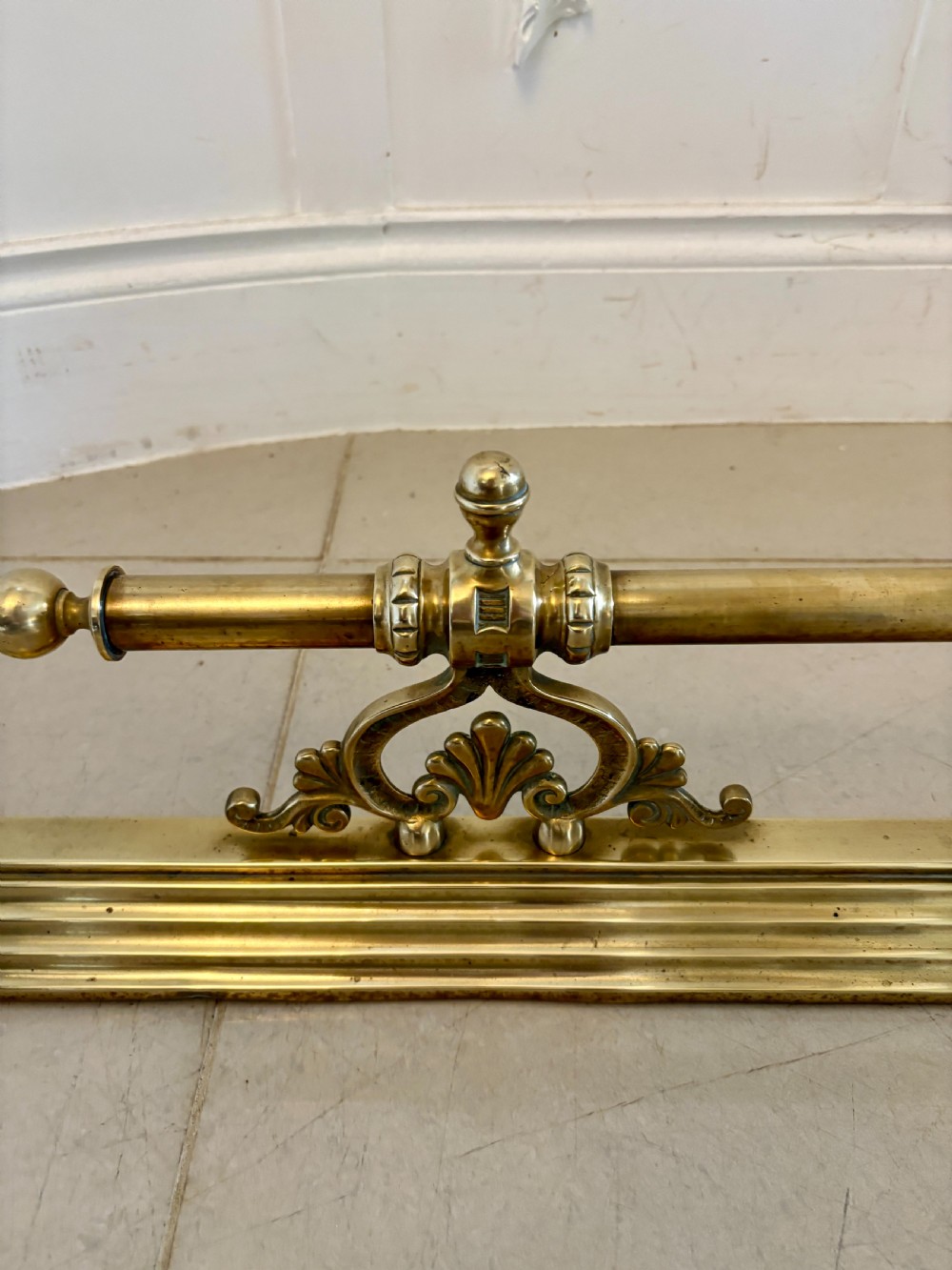 A Victorian brass fireplace fender featuring a low moulded base, fluted corner finials, and an elevated tool rail supported by scrolling brackets. View VII