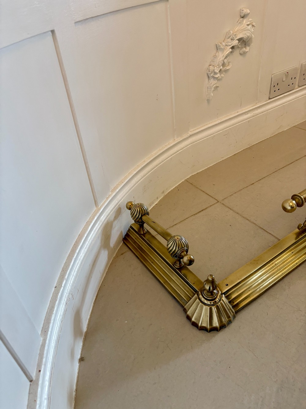 A Victorian brass fireplace fender featuring a low moulded base, fluted corner finials, and an elevated tool rail supported by scrolling brackets. View VIII