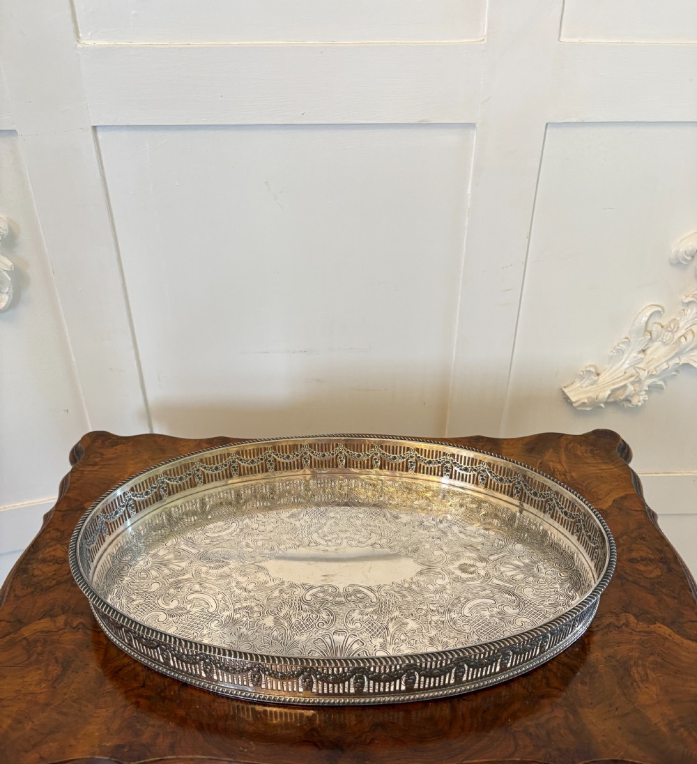 An oval antique Edwardian silver-plated gallery tray featuring intricate floral surface chasing and a raised pierced rim.
