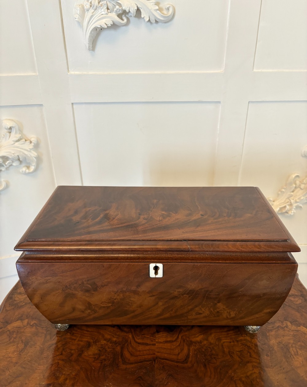 A Regency mahogany tea caddy featuring a hinged lid, tapered body, central escutcheon, and metal ball feet.